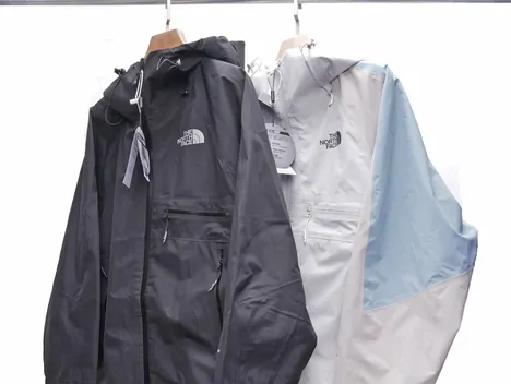 Two lightweight zip jackets hanging side by side, one charcoal and one pale grey with blue panels